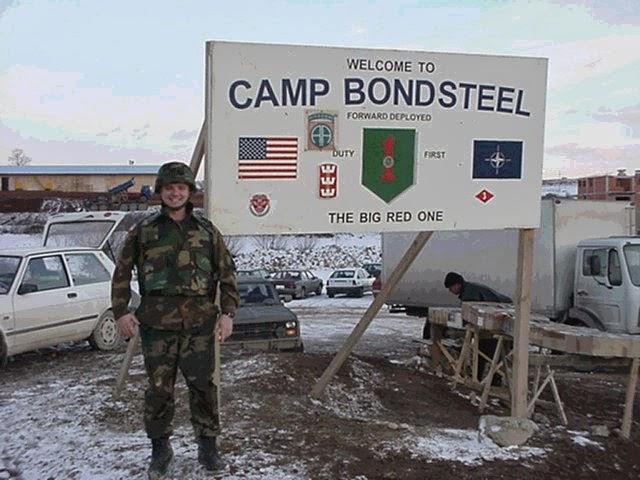 A person in military uniform standing in front of a sign Description automatically generated with low confidence