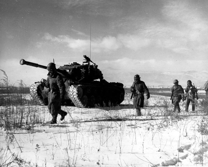 A group of soldiers walking next to a tank Description automatically generated
