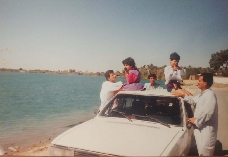 Feurat Alani and his sister sit atop a car parked on the banks of a river. Three uncles stand around them.