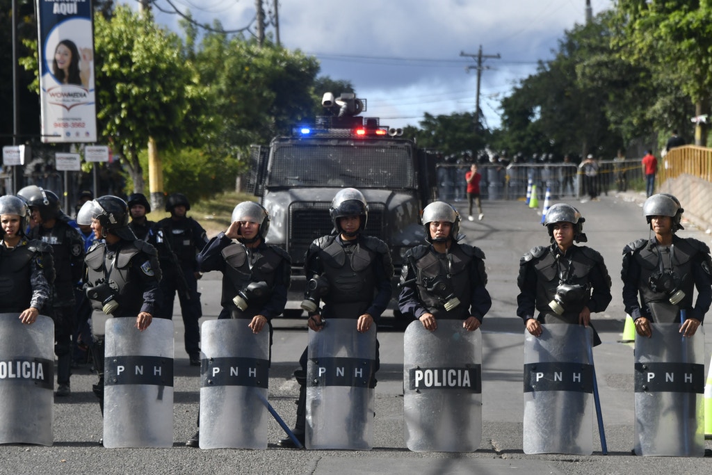 Honduran military police stand guard next to supporters of opposition candidate Salvador Nasralla as they hold a protest march on December 3, 2017 in Tegucigalpa, despite the state of emergency and a 10-day curfew imposed by the government to stop violent demonstrations triggered by claims of presidential election fraud. Honduras aims to resume the vote count to define the winner of the November 26 elections between President Juan Orlando Hernandez and the opposition candidate Salvador Nasralla. One young woman was killed and at least 12 civilians have been wounded during violent clashes sparked by Nasralla's call for his supporters to take to the streets. / AFP PHOTO / JOHAN ORDONEZ (Photo credit should read JOHAN ORDONEZ/AFP/Getty Images)