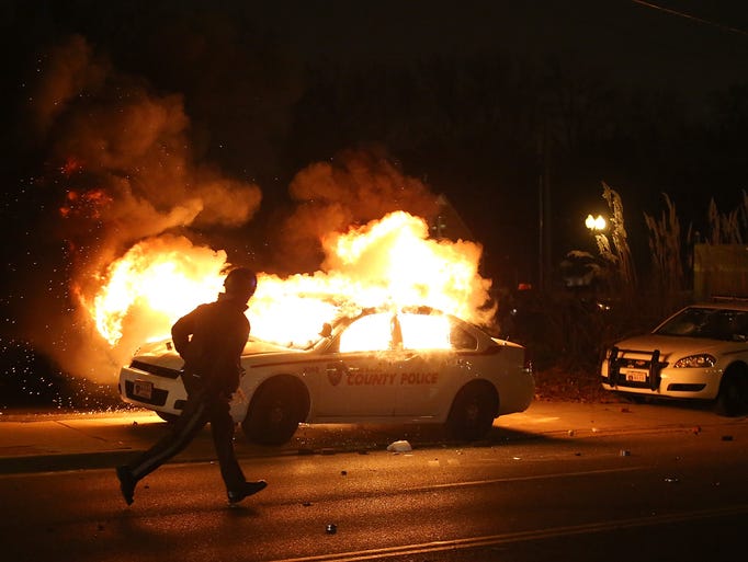 A police officer runs by a burning police car during